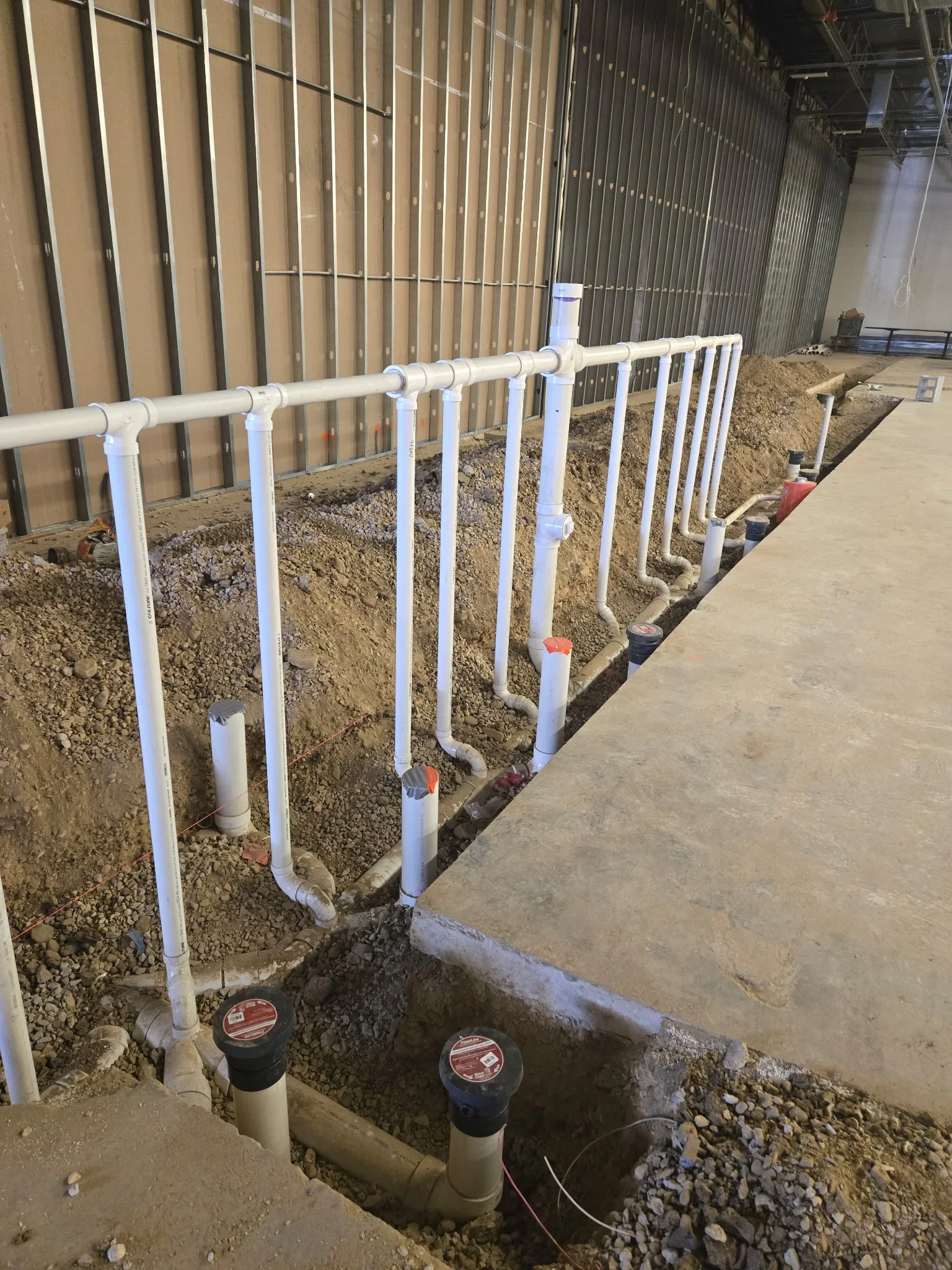 White PVC plumbing pipes with fittings and cleanout caps installed in commercial building trench