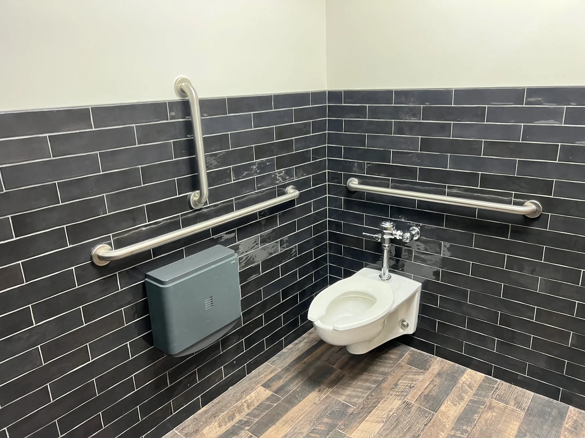 Accessible bathroom with wall-mounted toilet, chrome grab bars, and black subway tile walls