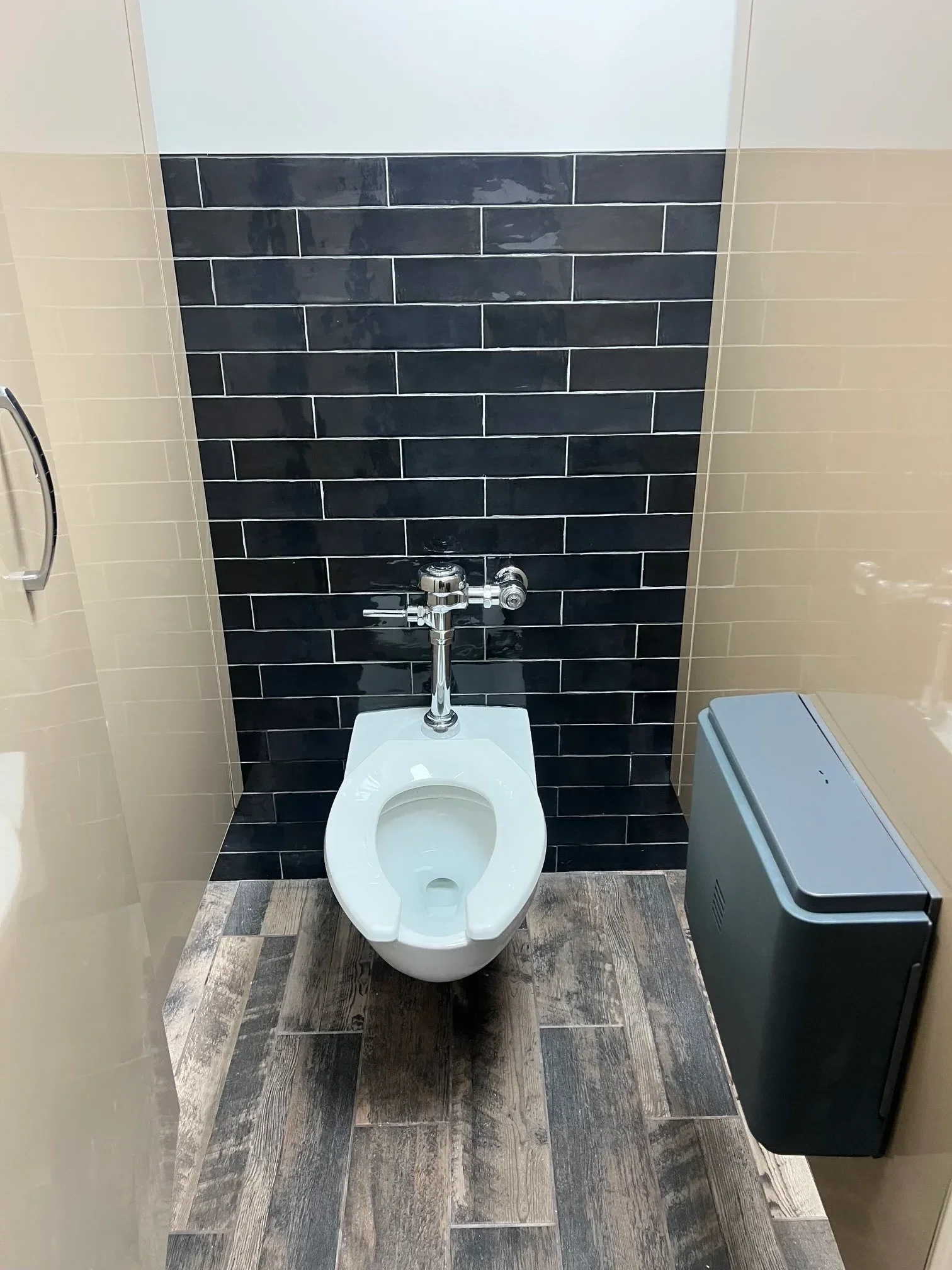 White porcelain toilet with chrome valve installed in bathroom with black subway tile and wood-grain ceramic accents