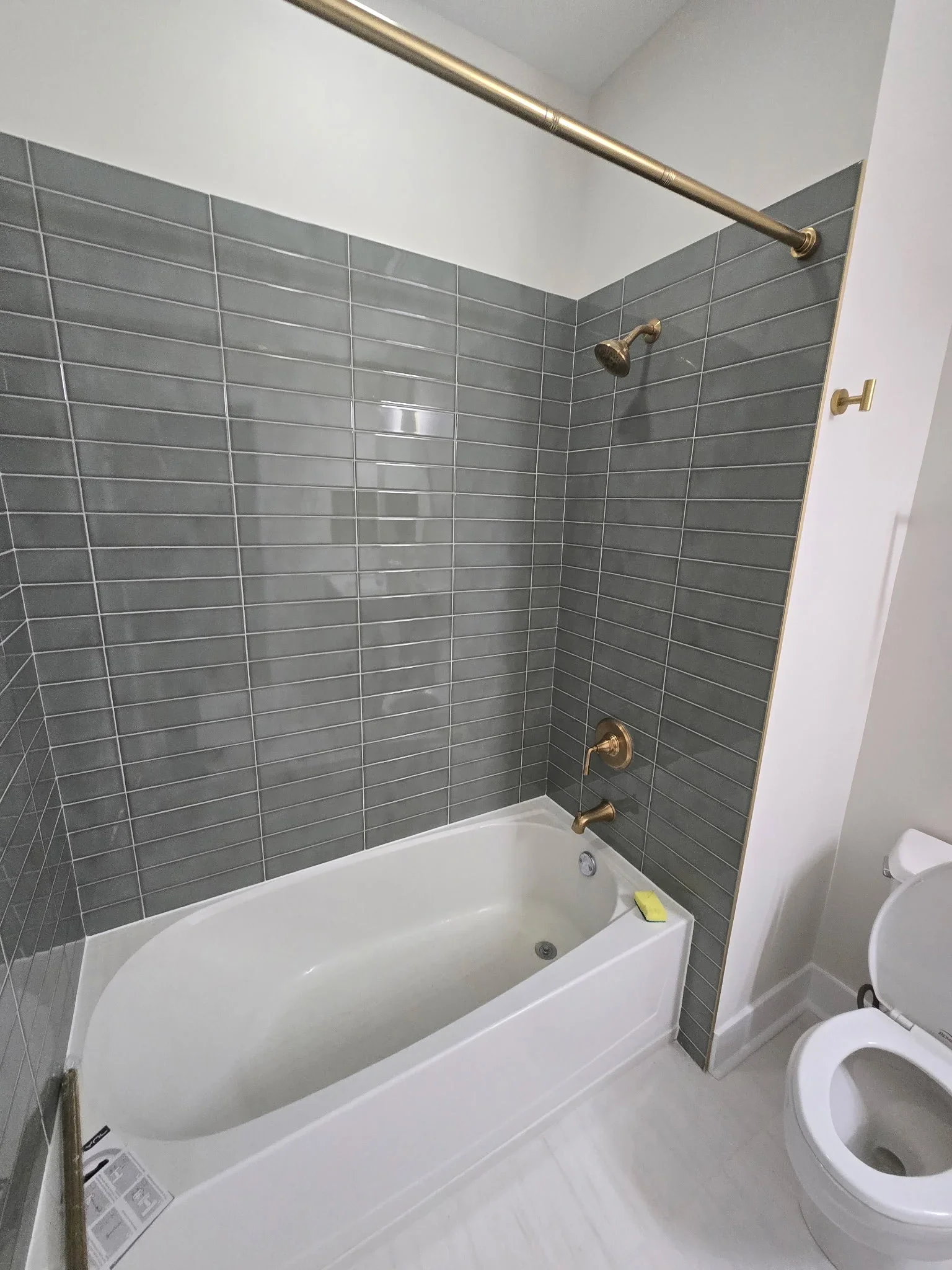 White bathtub with brass fixtures and gray subway tile surround in bathroom