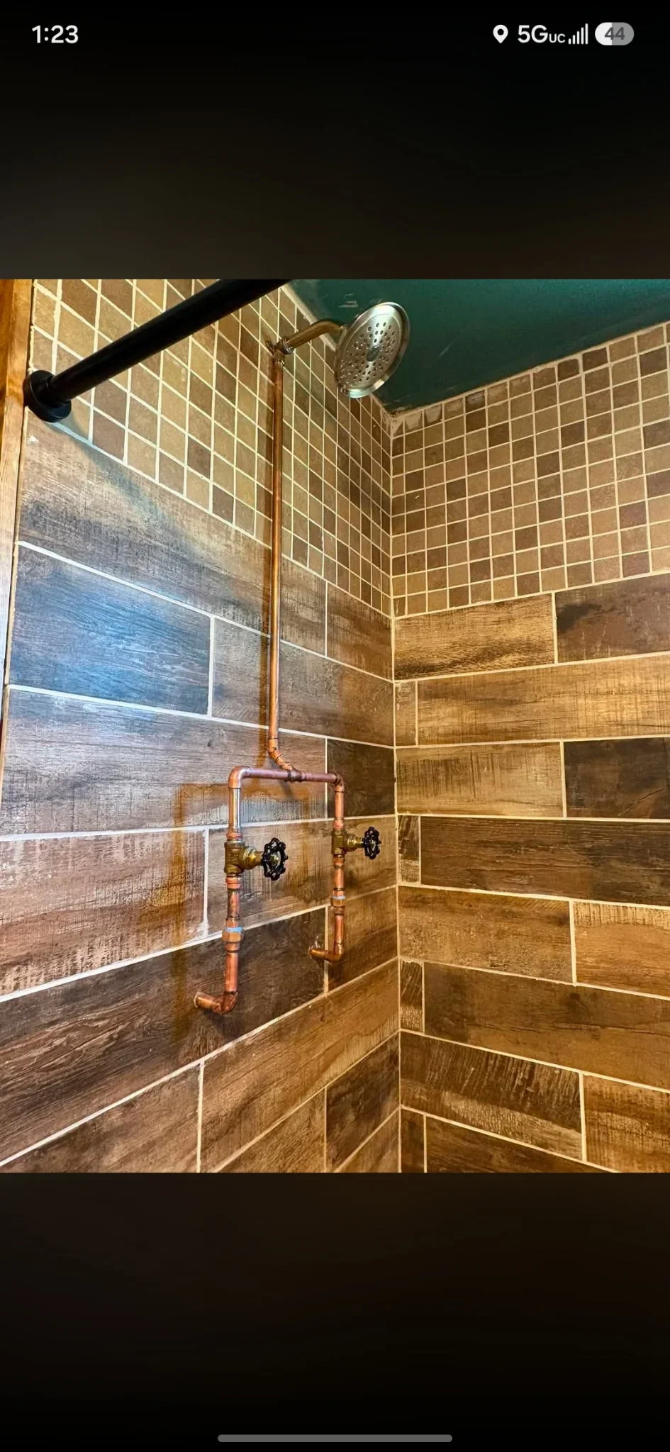 Shower stall with wood-grain tile walls, copper piping, and rainfall showerhead