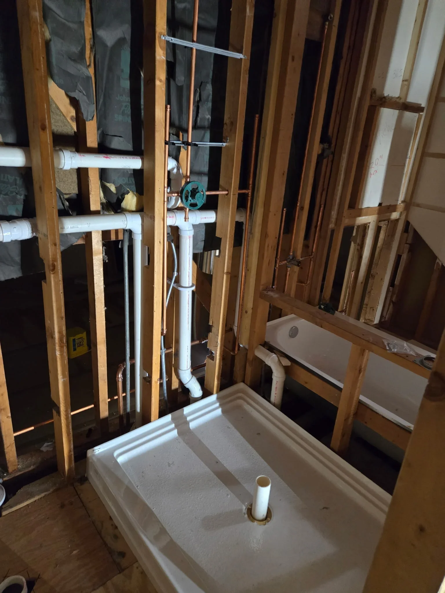 PVC plumbing rough-in with drain lines, supply pipes, shutoff valve, and venting stack in framed bathroom