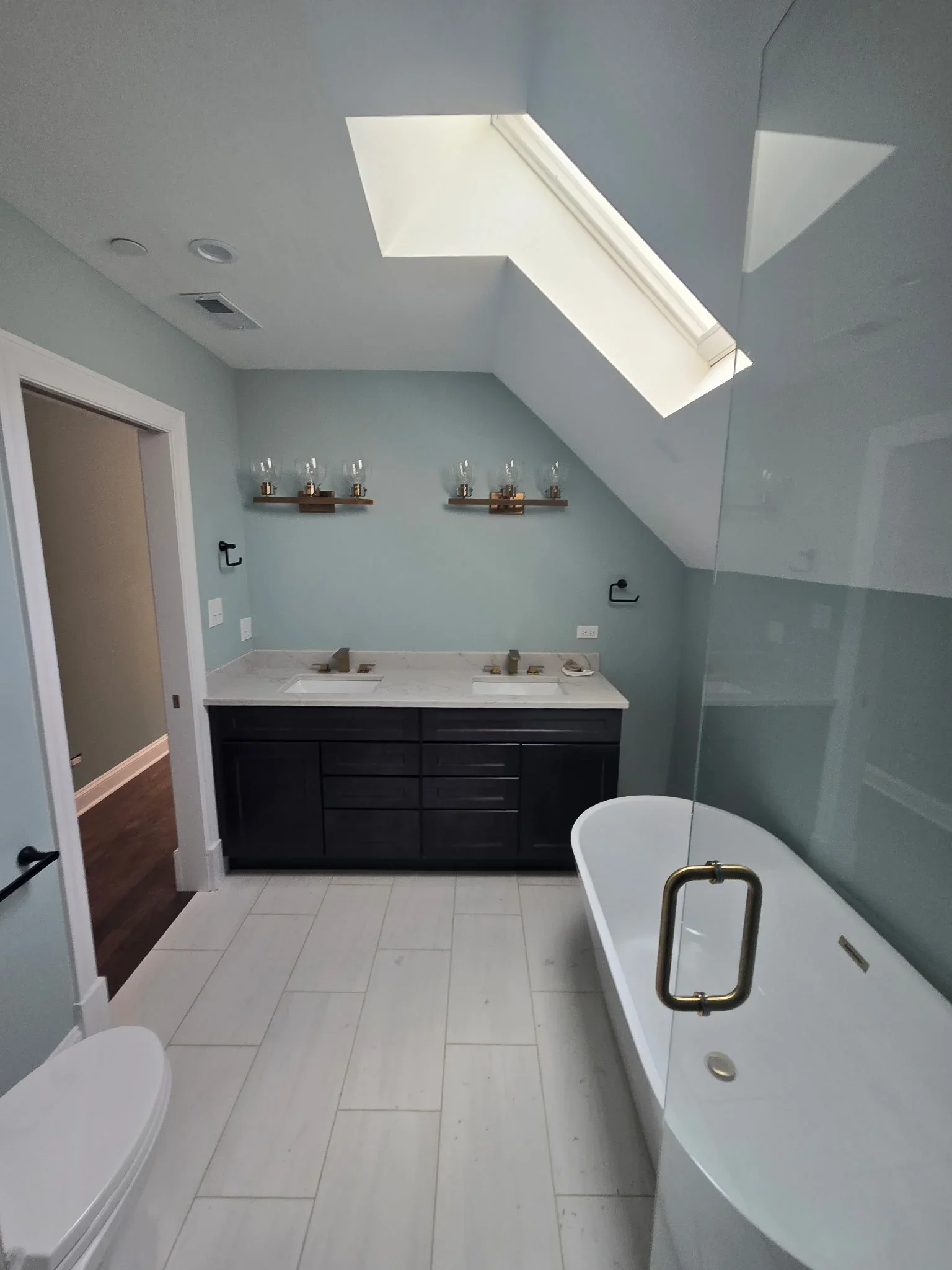 Dual vanity with white quartz countertop, black cabinetry, brass faucets, and freestanding tub