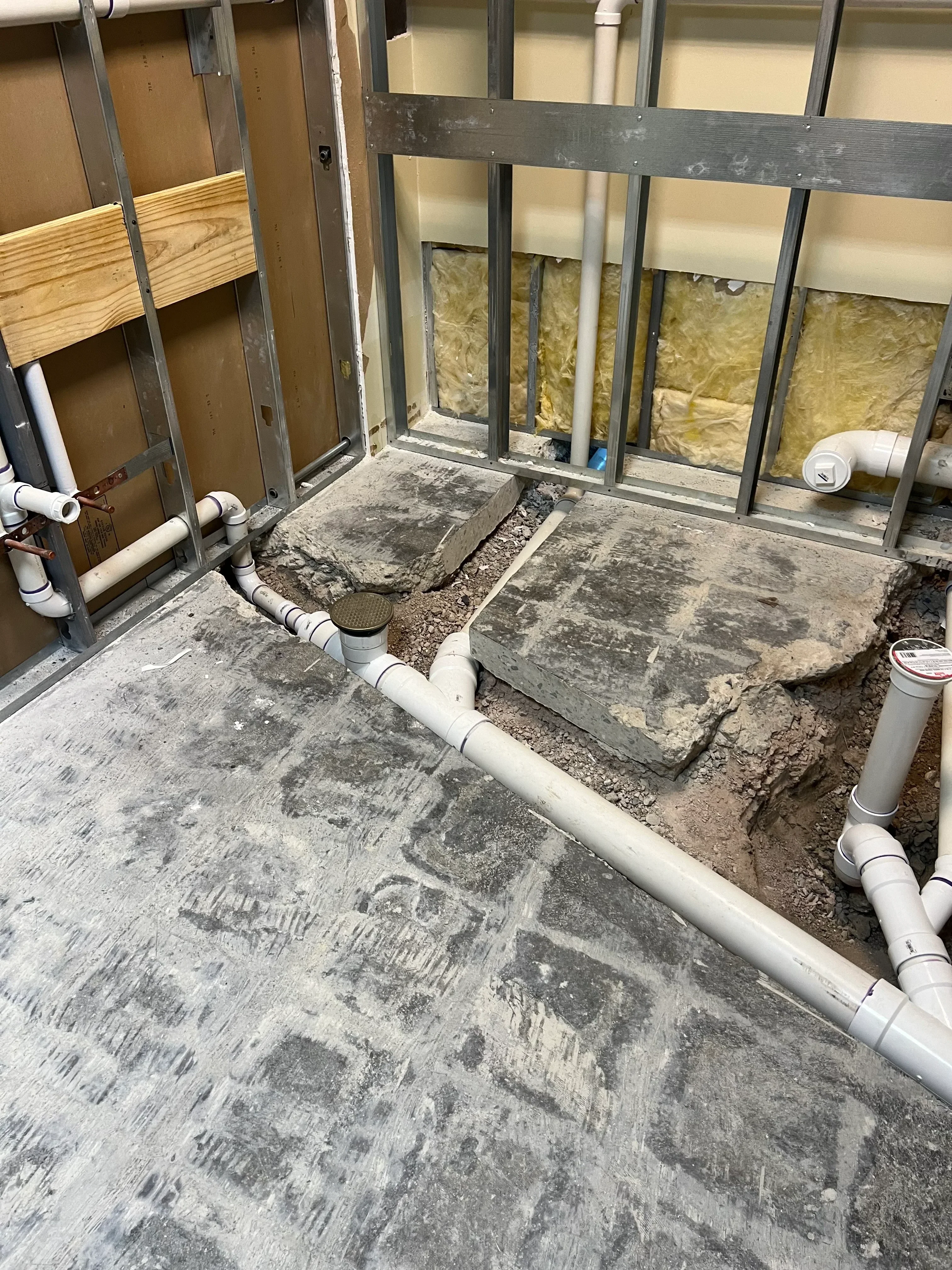 White PVC drain pipes and vent stacks installed in basement with steel framing and yellow insulation batts