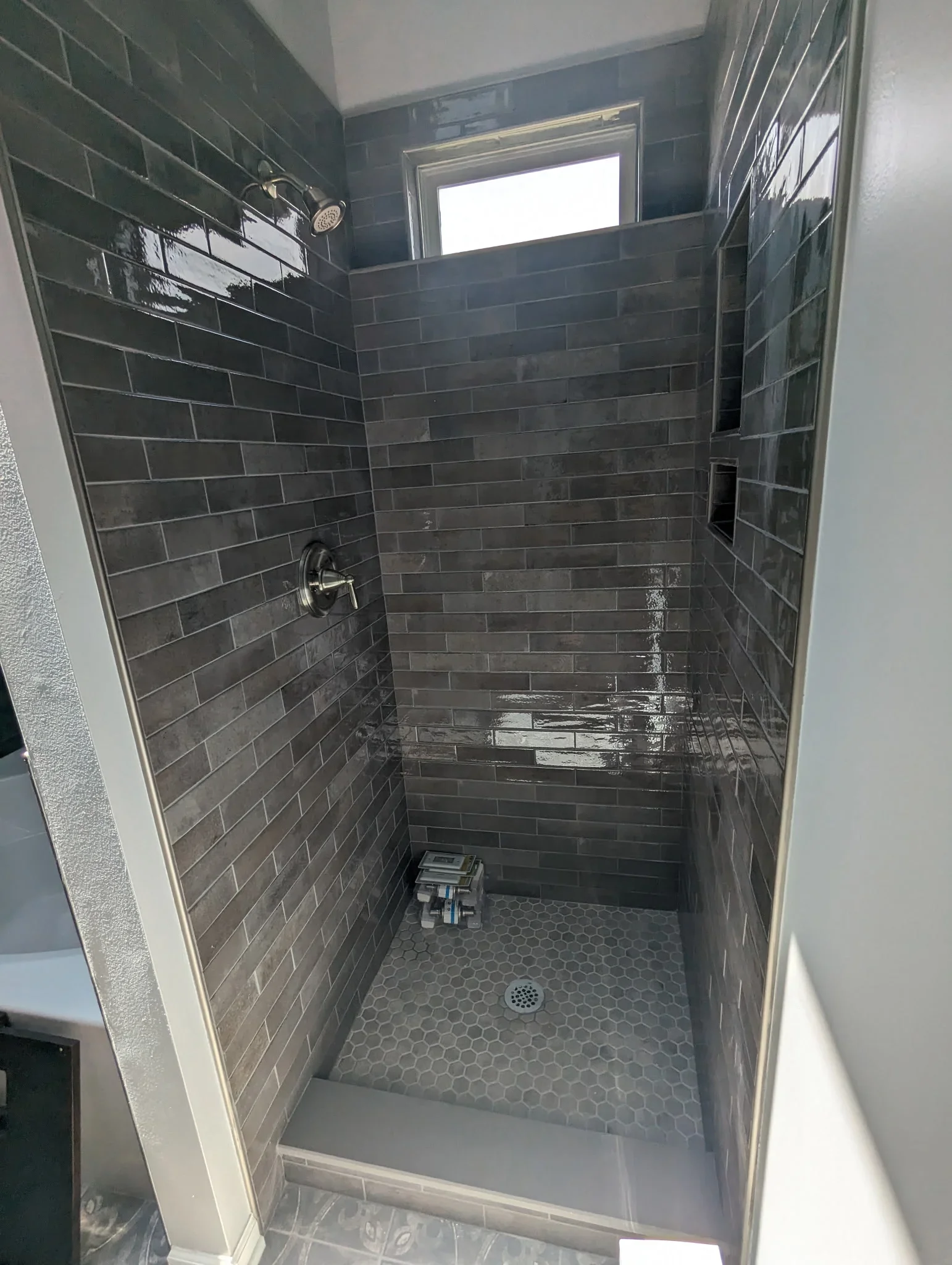 Charcoal subway tile shower with hexagon floor, chrome fixtures, and recessed niche