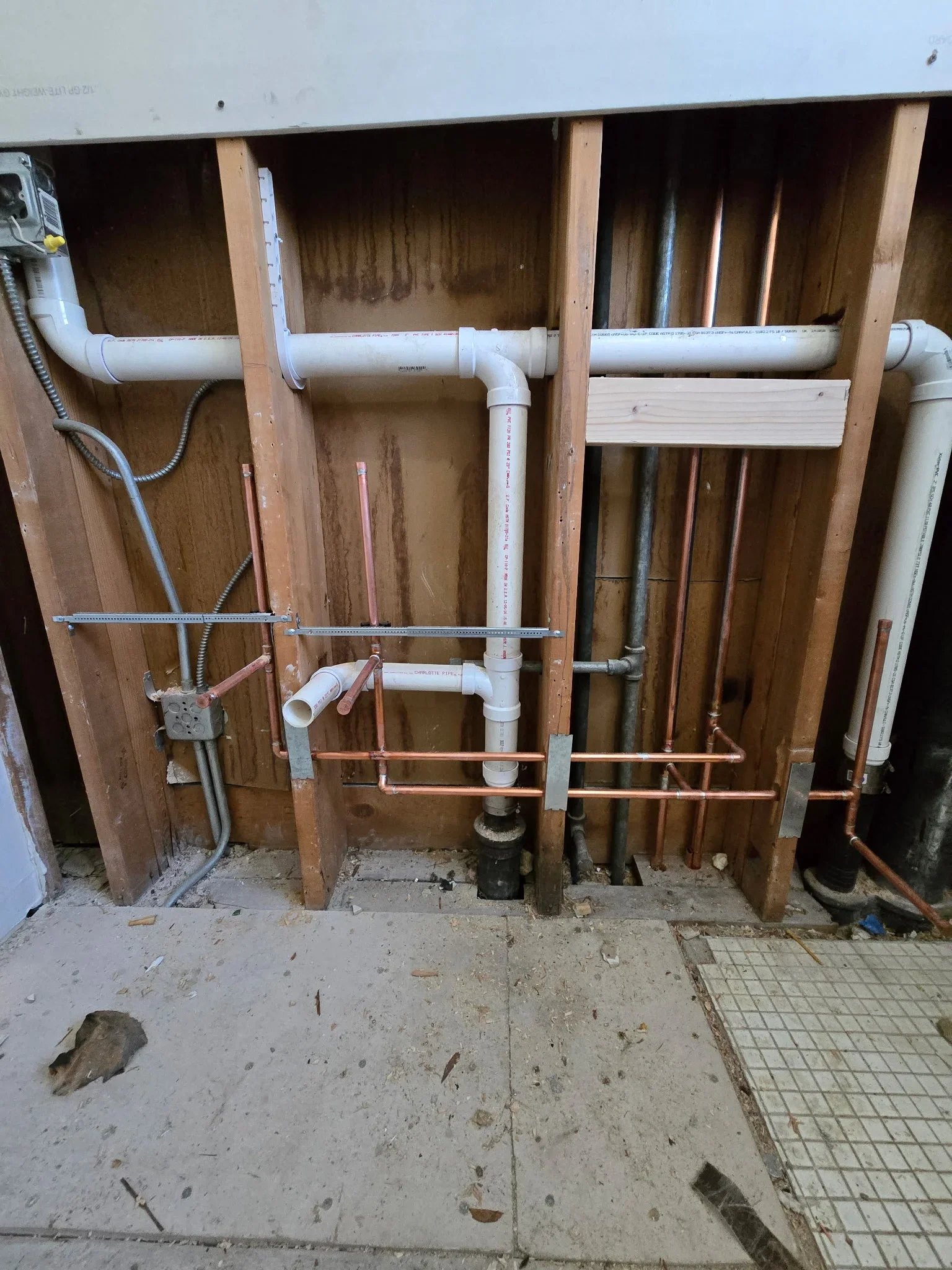 Rough-in plumbing with PVC drains, copper and PEX supply lines in framed wall cavity