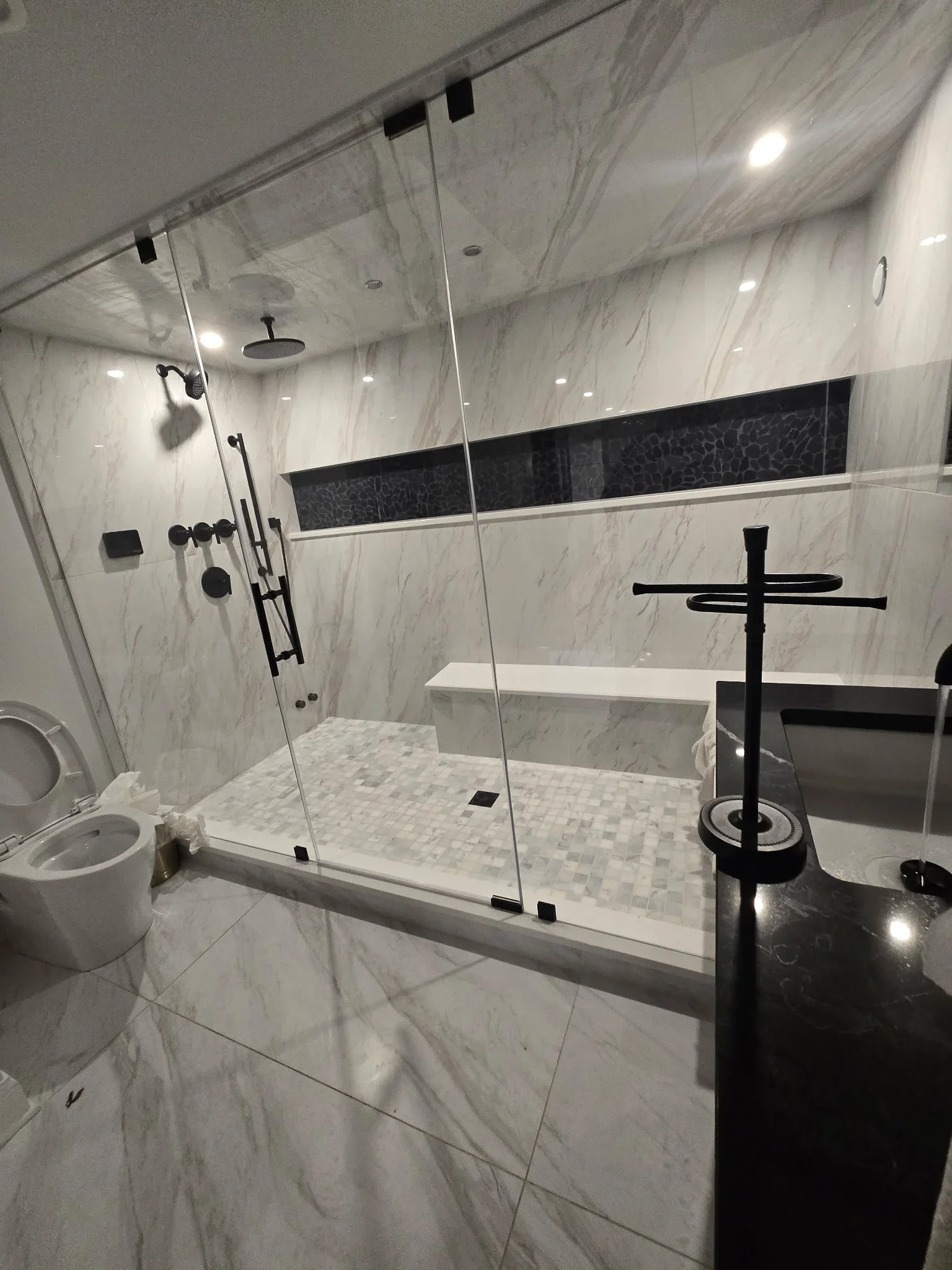 Marble tile shower with frameless glass doors, black matte fixtures, and mosaic floor