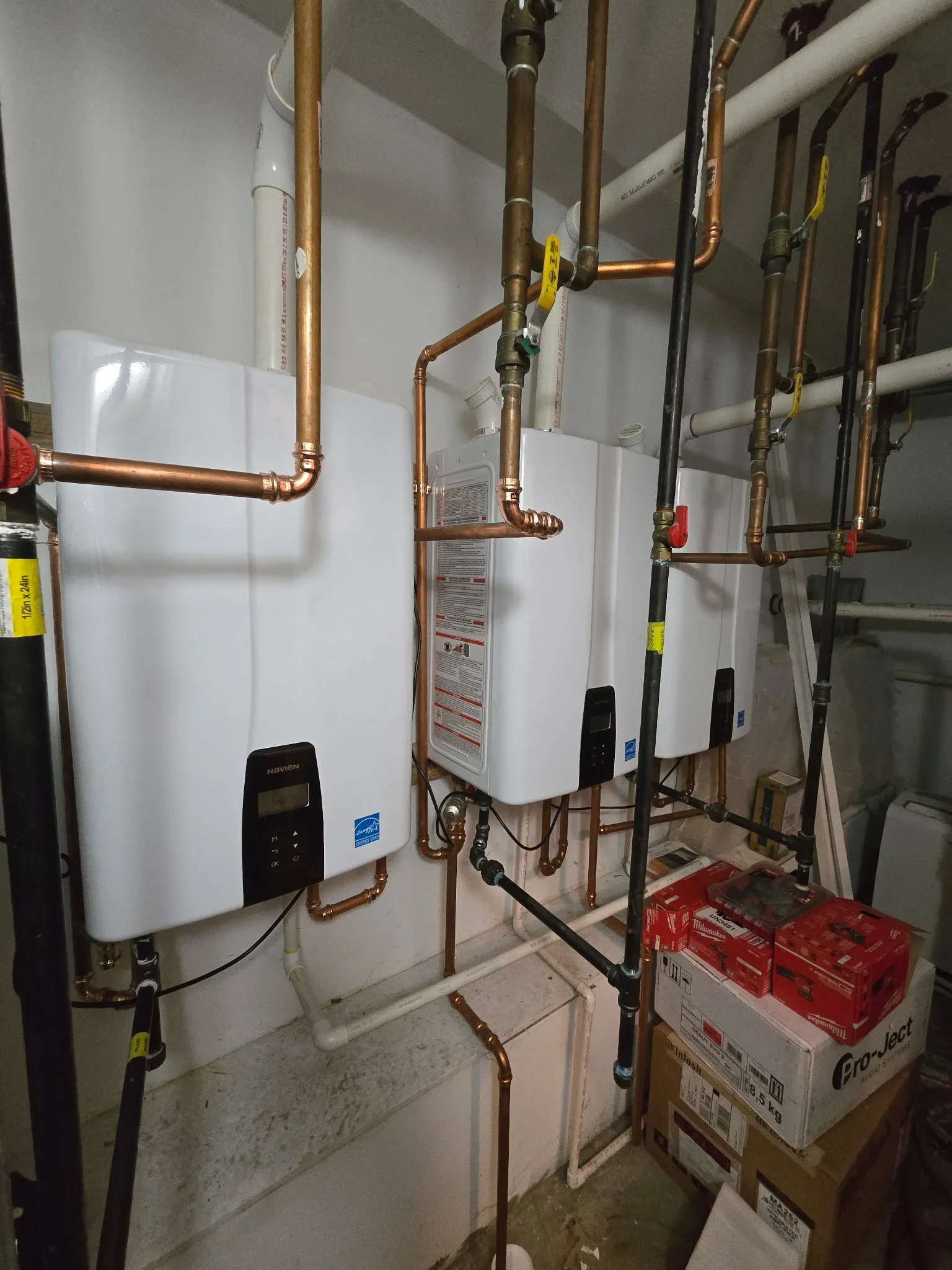 Multiple white tankless water heaters with copper piping, valves, and control panels installed on wall
